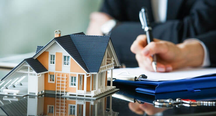 Un homme lit les termes de son contrat d’assurance et prend des notes derrière la maquette d’une maison