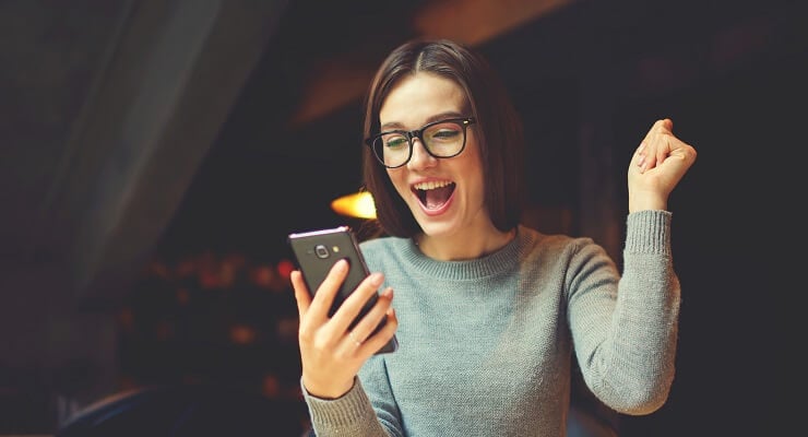 Une jeune femme s'exclame de joie devant l'écran de son téléphone mobile