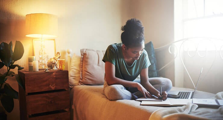 Une jeune femme lit et écrit dans sa chambre près d’une lampe
