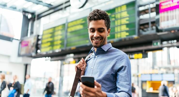 Un homme d'affaires regarde son téléphone mobile devant le tableau des départs dans une gare