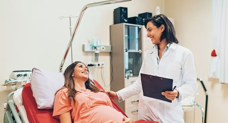 Une femme enceinte allongée sur un lit d'hôpital sourit à sa médecin